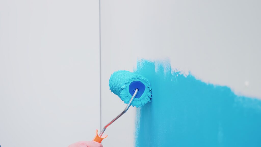 roller brush wall with blue paint apartment redecoration home construction while renovating improving repair decorating